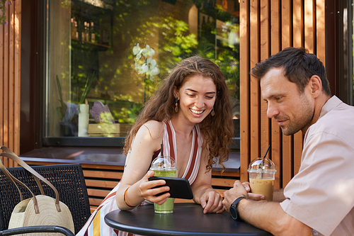 Portrait of happy couple at outdoor cafe looking at smartphone screen while enjoying date in Summer, copy space
