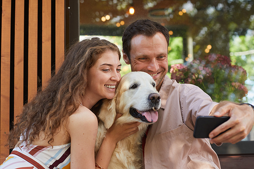 Portrait of young couple taking selfie with dog outdoors in Summer, copy space