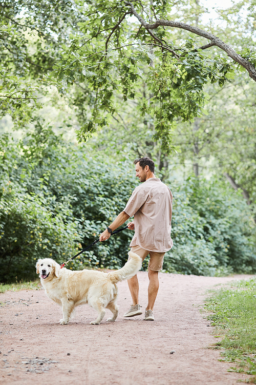 Vertical full length portrait of happy adult man walking dog in park in Summer, copy space
