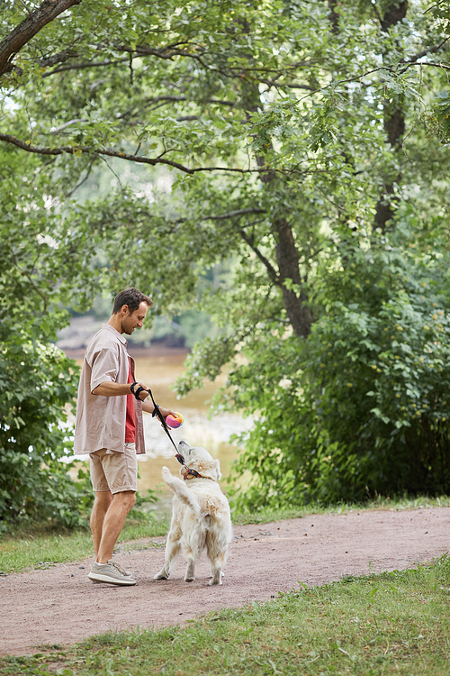 Vertical full length portrait of smiling man walking dog in green park in Summer