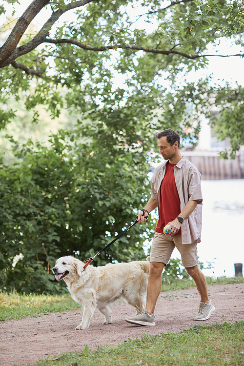Vertical full length portrait of smiling man walking dog outdoors in Summer at green park