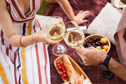 Top view close up of young couple holding wine glasses while enjoying romantic picnic outdoors, copy space