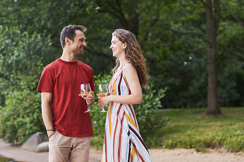 Side view portrait of happy couple holding wine glasses while enjoying romantic date outdoors, copy space