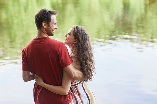 Back view portrait of happy young couple embracing while enjoying romantic date outdoors by water, copy space