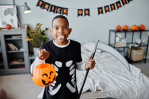 Waist up portrait of teenage African-American boy holding Halloween bucket while making faces at camera indoors, copy space