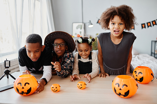 Group of African-American kids dressed in Halloween costumes posing with pumpkin pails indoors and looking at camera