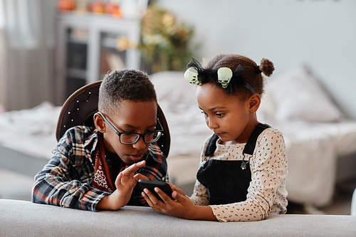 Front view portrait of two African-American kids using smartphone together in cozy home interior, copy space