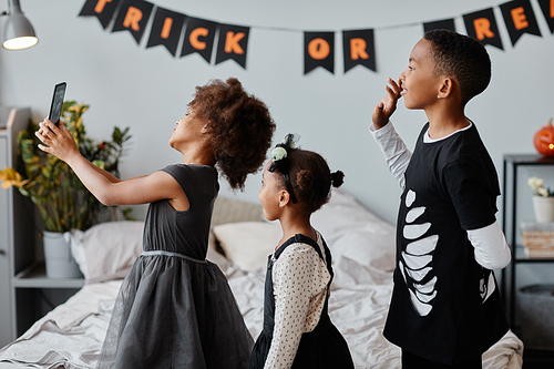 Side view portrait of cute African-American children wearing Halloween costumes at home and waving at camera while video chatting with family