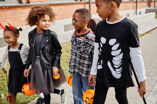 Group of excited African-American kids wearing Halloween costumes outdoors while trick or treating together