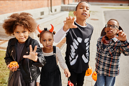 Group of African-American kids wearing Halloween costumes and posing for camera while trick or treating together