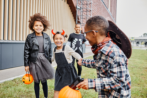 Group of cheerful African-American kids wearing Halloween costumes and running towards camera while trick or treating together