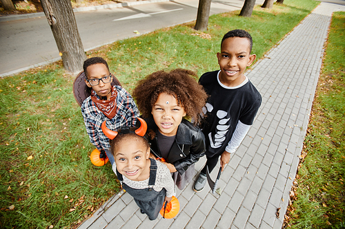 Group of smiling African-American kids trick or treating outdoors and looking up at camera, copy space