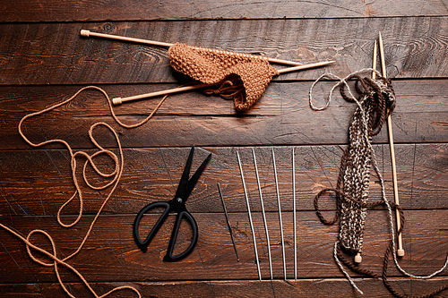 Top down flatlay of wool and knitting supplies on dark wooden background, copy space