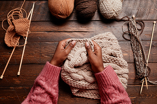 Top view close up of female hands knitting against dark wooden background, copy space