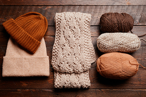 Top down view of knit scarf and hat with wool on dark wooden background, knitting and hobby, copy space