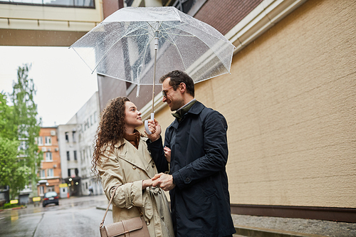 Horizontal medium portrait of Caucasian man and woman spending time together outdoors walking under umbrella and chatting