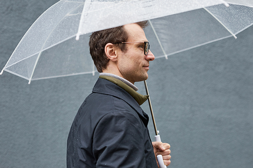 Side view medium close-up shot of stylish mature Caucasian man wearing eyeglasses standing under umbrella on rainy day