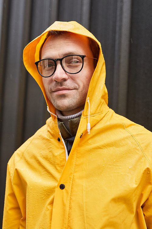 Vertical medium close-up shot of mature man wearing yellow raincoat standing outdoors on rainy day looking at camera