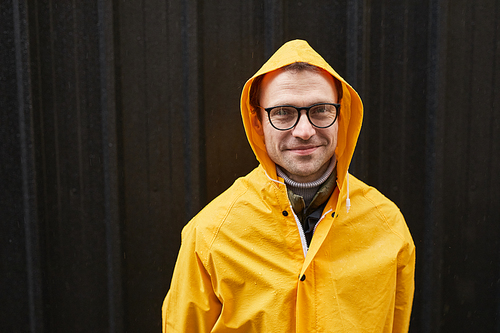 Horizontal medium close-up shot of Caucasian man wearing yellow raincoat standing outdoors on rainy day looking at camera