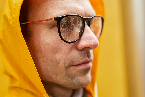 Close-up portrait of modern Caucasian man wearing yellow raincoat standing outdoors looking away