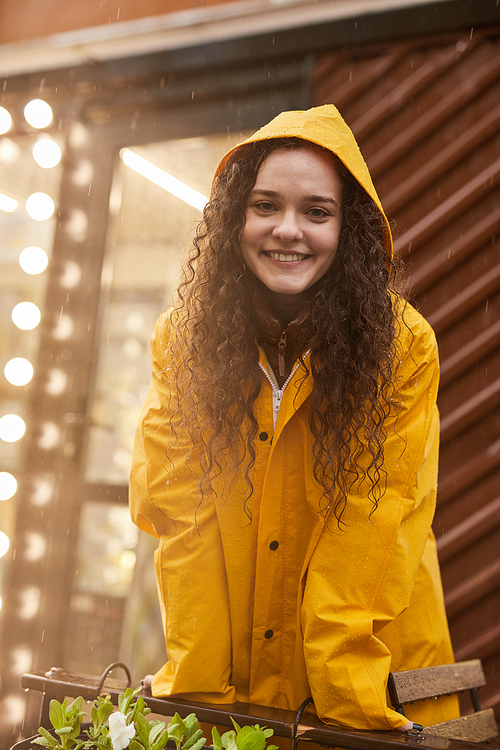 Vertical medium shot of attractive Caucasian woman wearing yellow raincoat standing in rain smiling at camera