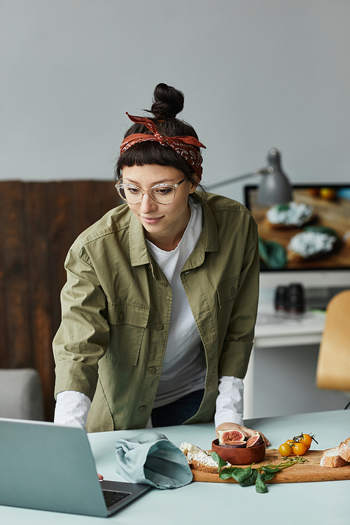 Vertical portrait of female food photographer using laptop while setting up scene in studio