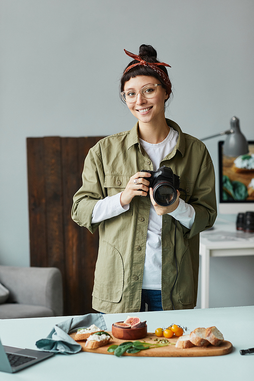 Vertical portrait of young female photographer smiling at camera while posing in studio