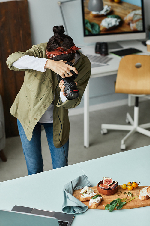 Vertical portrait of female food photographer taking pictures while working in home studio