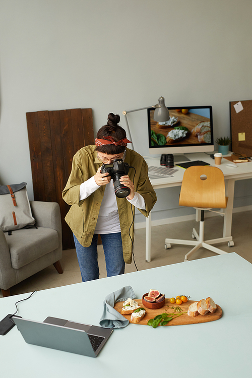 Vertical shot of female food photographer taking pictures while working in home studio