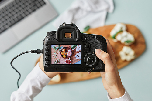 Top view close up of food photographer holding digital camera with image on screen while working in home studio, copy space