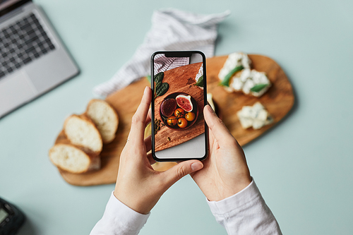 Top view of young woman taking aesthetic photo of food using smartphone in home studio, copy space