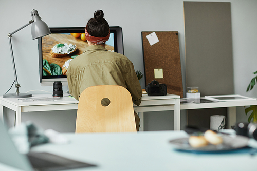 Back view of female food photographer using computer while retouching photos in studio, copy space