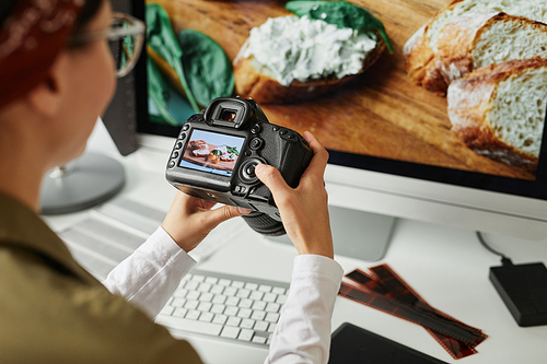 High angle view at female photographer holding camera with image on screen while editing photos at workplace