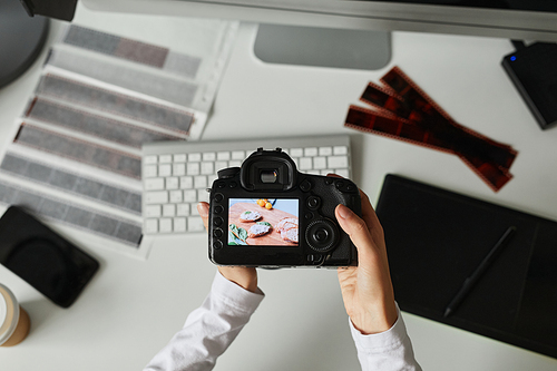 Top view closeup of female photographer holding camera with image on screen while editing photos at workplace