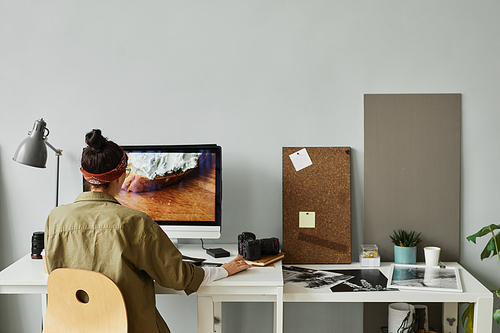 Minimal back view of female photographer editing photos at workplace in studio, copy space