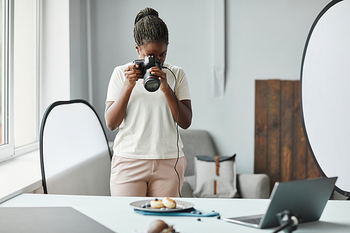 Minimal portrait of young African American woman taking food photography pictures in studio, copy space