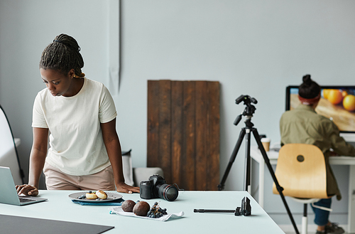 Portrait of young African American woman using laptop while working with food photography in studio, copy space