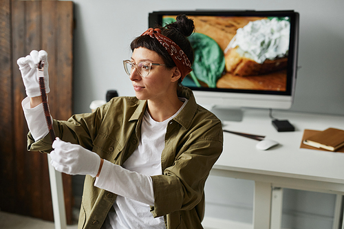 Portrait of young female photographer holding film roll in studio while wearing cotton gloves, copy space