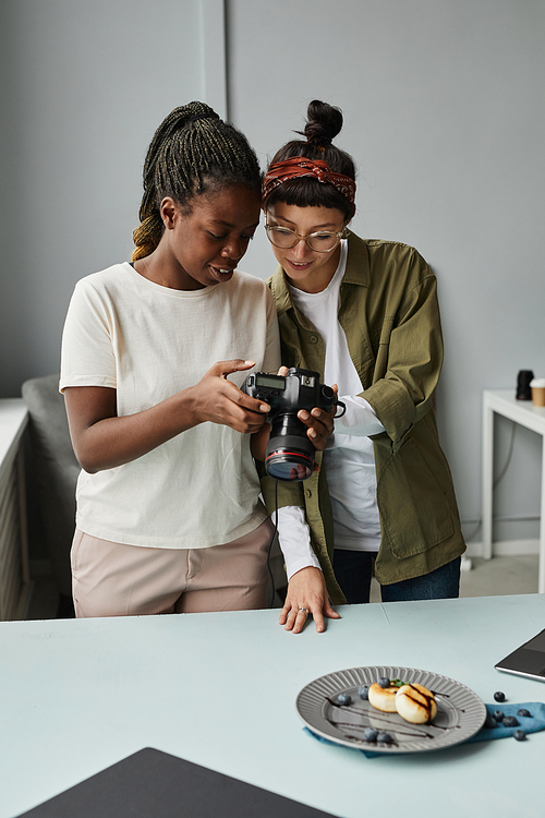 Vertical portrait of two female photographers looking at photos in camera while working at photo studio