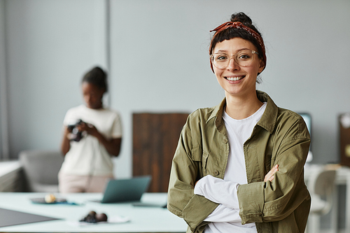 Waist up portrait of young female photographer smiling at camera while standing in photo studio, copy space