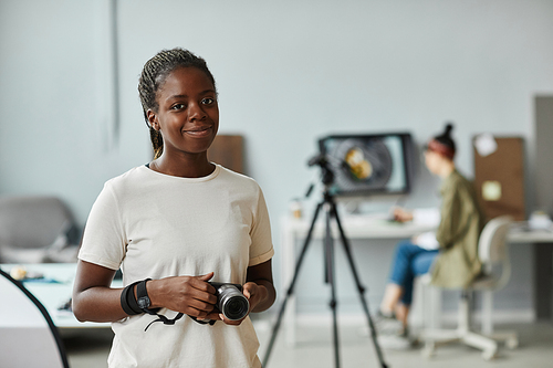 Waist up portrait of young African American woman smiling at camera while standing in photo studio, copy space