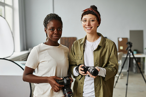 Waist up portrait of two female photographers smiling at camera while standing in photo studio, copy space