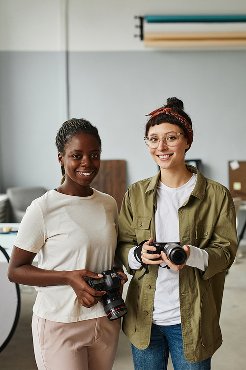 Vertical portrait of two female photographers smiling at camera while standing in photo studio