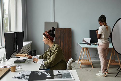 Side view portrait of young female photographer using computer for photo retouch while working in studio, copy space