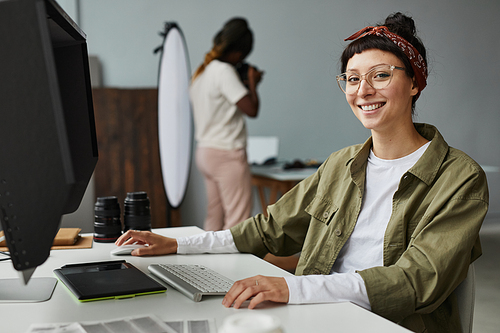 Portrait of smiling female photographer looking at camera while using computer at workplace in photo studio