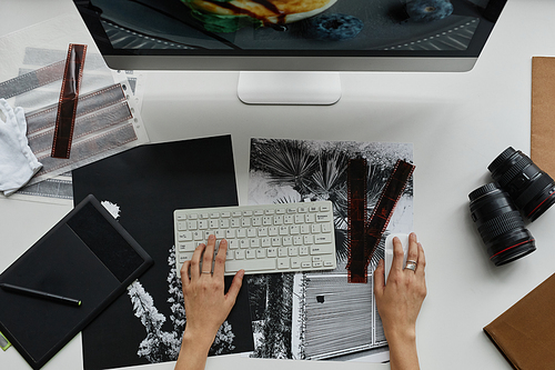 Top view close up of unrecognizable photographer editing photos at workplace in studio, focus on hands using keyboard