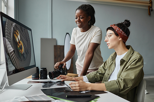 Portrait of two female photographers discussing images on computer screen while working on editing in studio