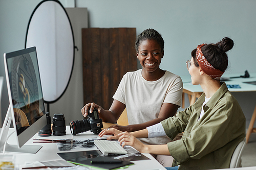 Portrait of two smiling female photographers collaborating while using computer in studio