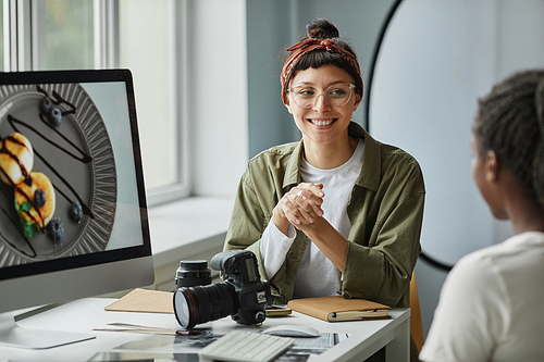 Portrait of smiling female photographer collaborating with colleague or client while discussing images in studio