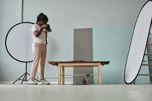 Minimal side view portrait of young African American photographer taking still life pictures in photo studio, copy space